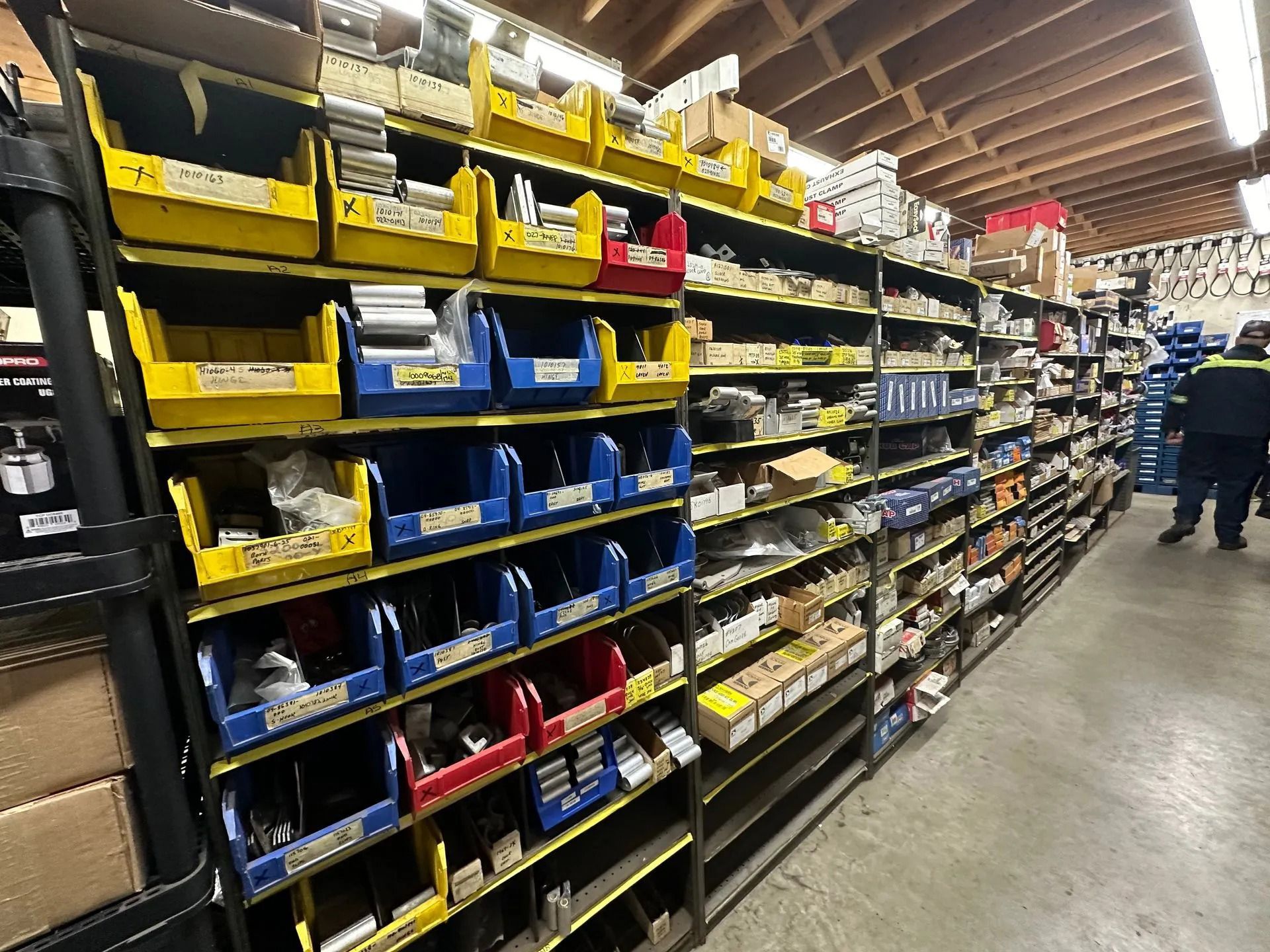 Industrial storage racks filled with yellow and blue bins, with an employee standing in the background aisle.