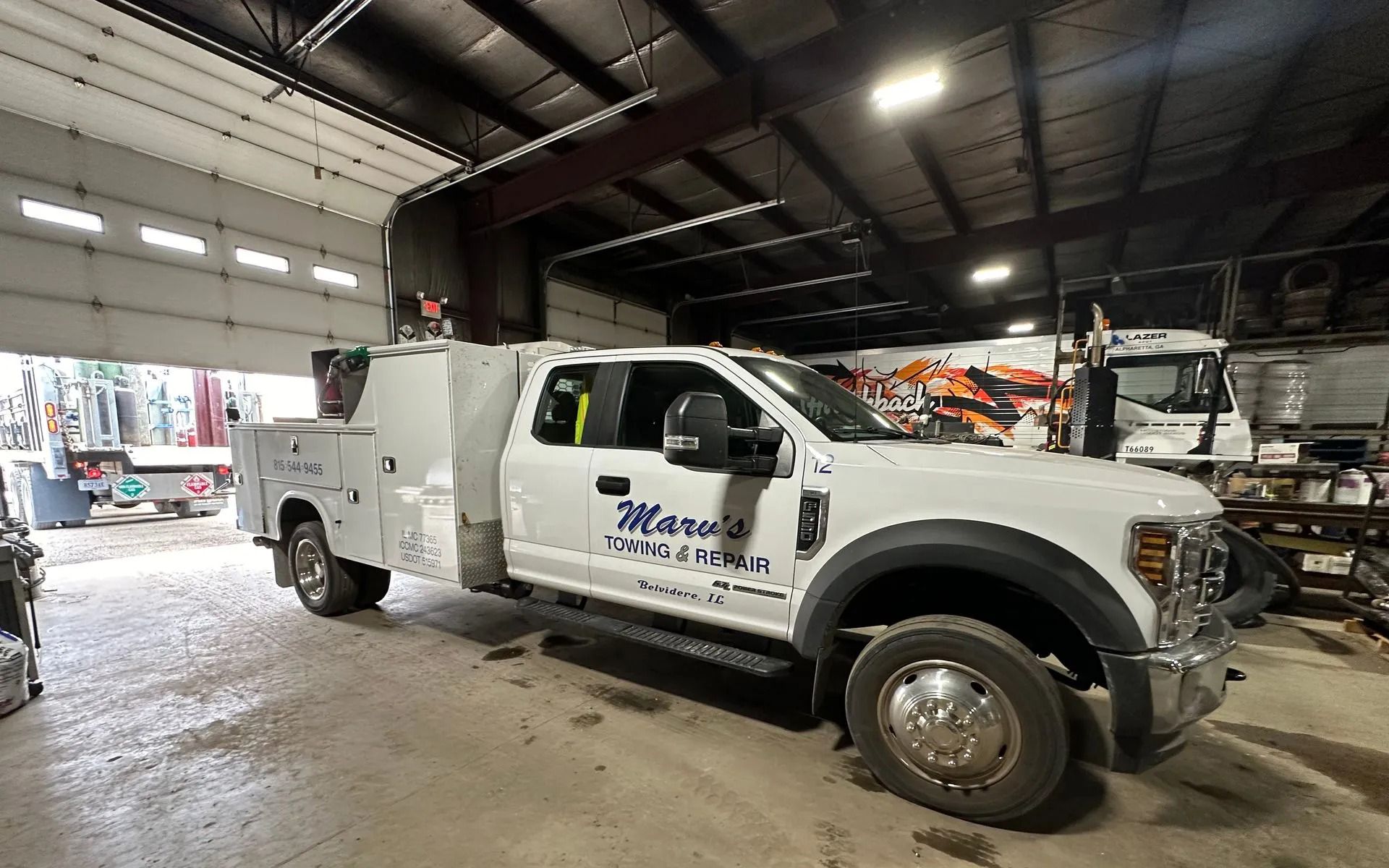 A white service truck with business branding parked inside a large, open-door maintenance garage.