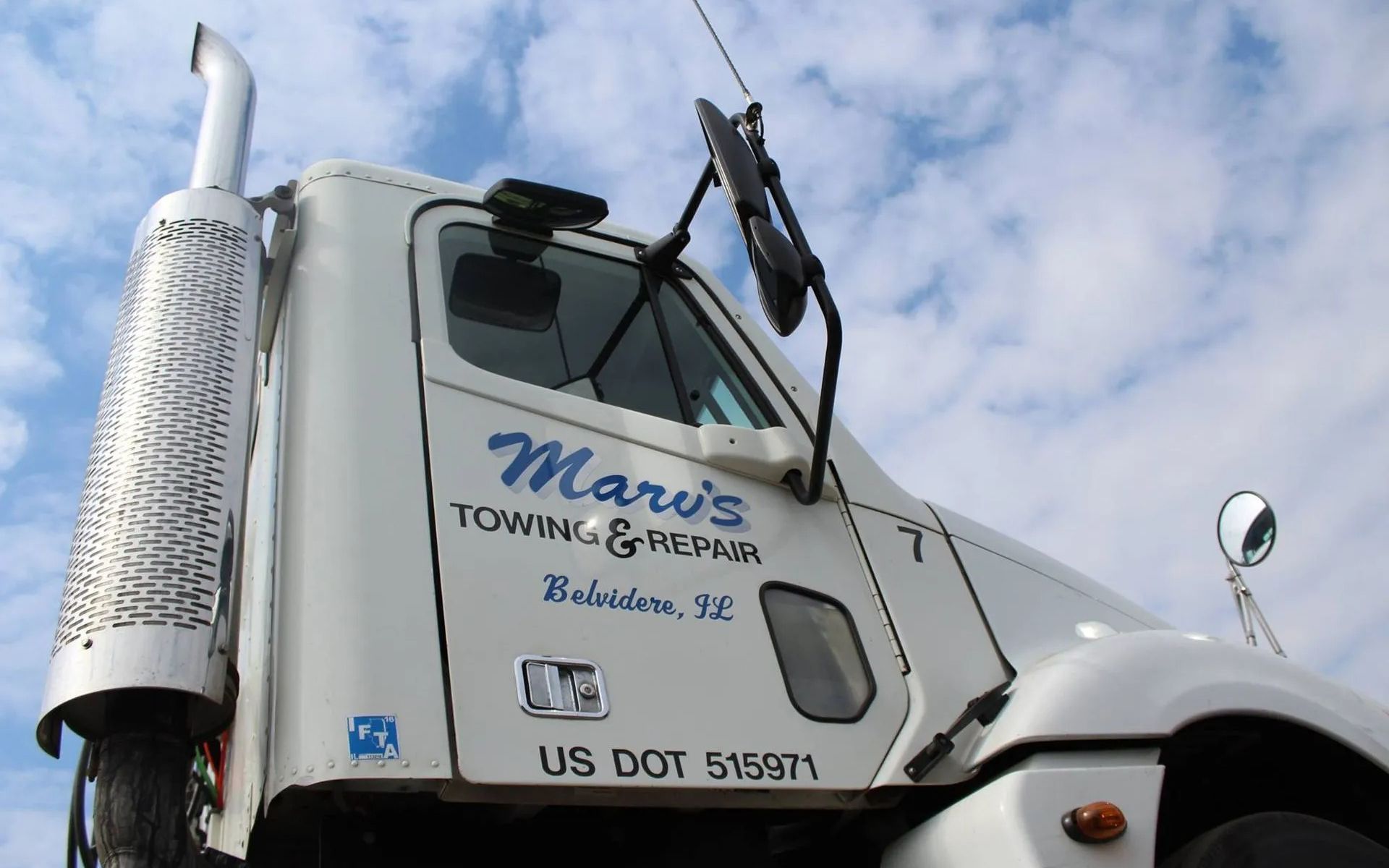 A white tow truck cab parked outdoors under a partly cloudy sky, with
