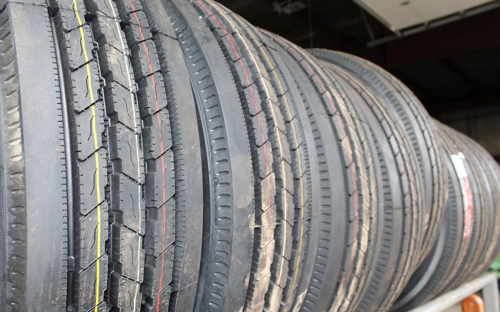 A row of new, black rubber semi-truck tires with yellow and red tread stripes, stacked vertically on a rack.