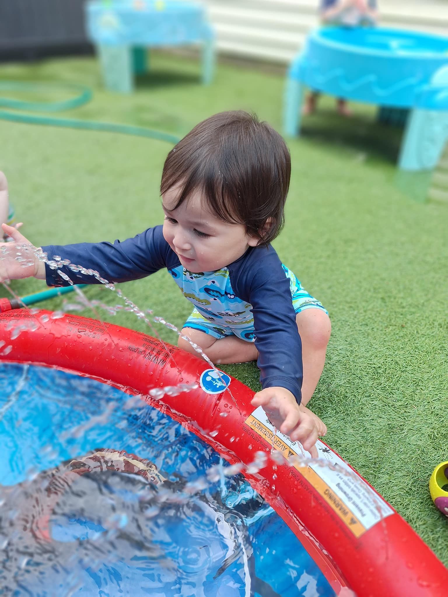 Child playing in a red and blue inflatable pool, splashing water.