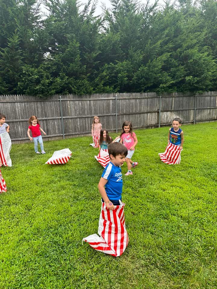 Children playing a sack race in a grassy backyard, some in striped sacks.