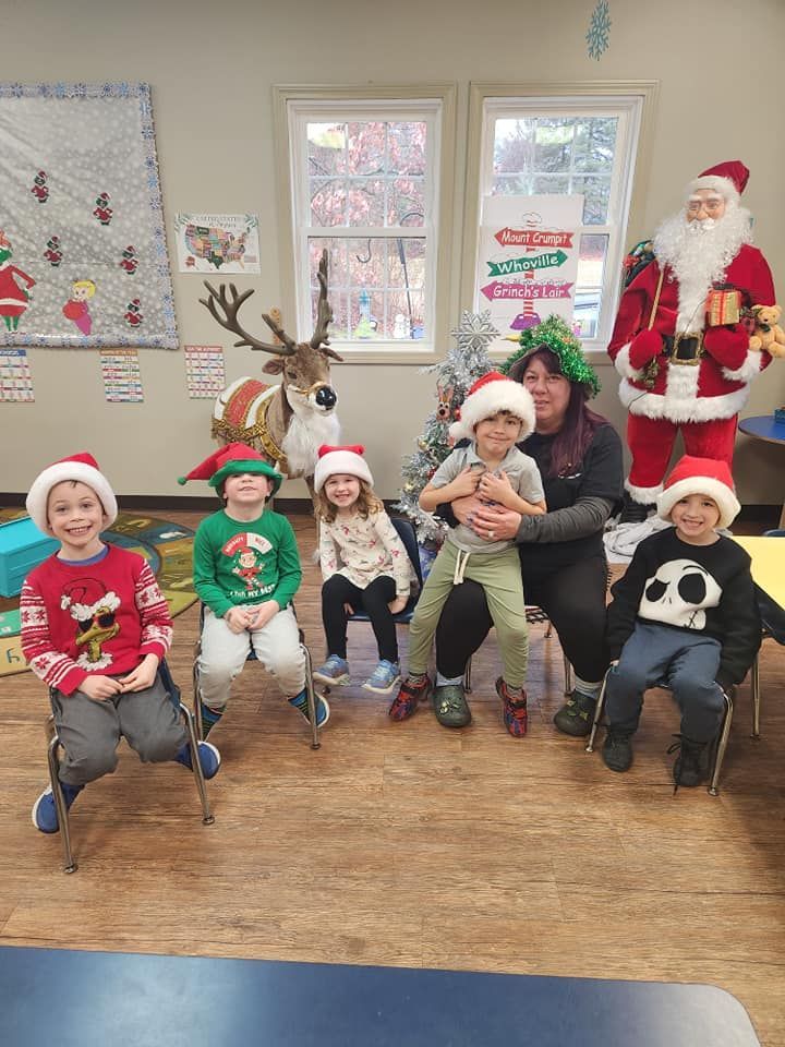 Children and an adult wearing Santa hats pose with Christmas decorations in a classroom.