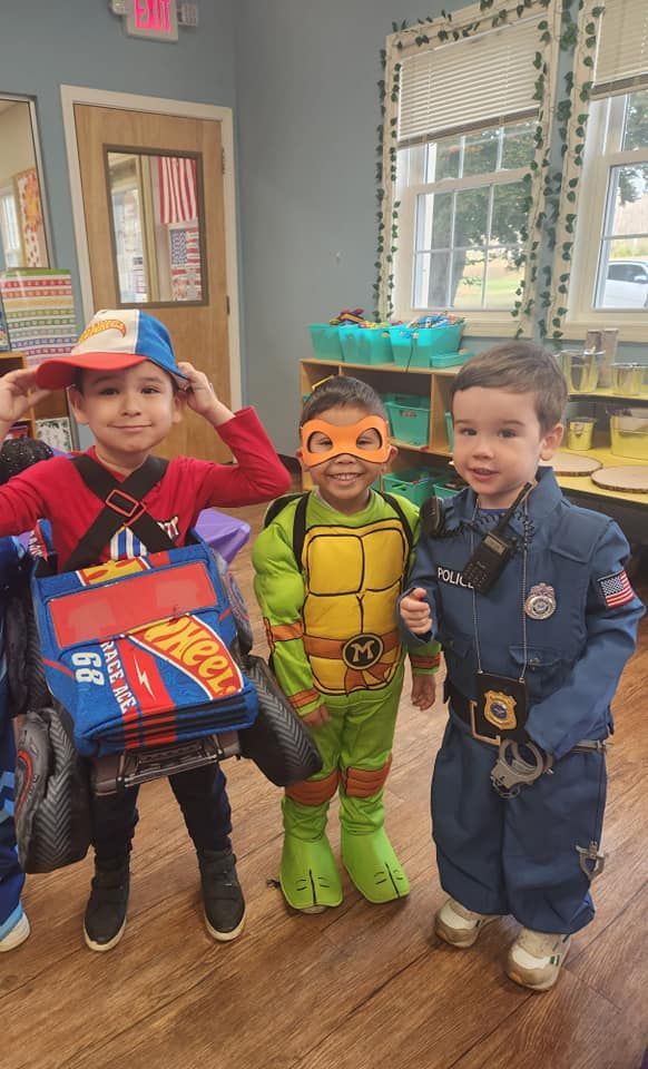 Three children in costumes: race car driver, Ninja Turtle, and police officer, smiling indoors.