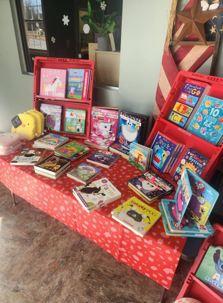 Books displayed on a table and in red crates. Books include children's stories with animals and colorful illustrations.