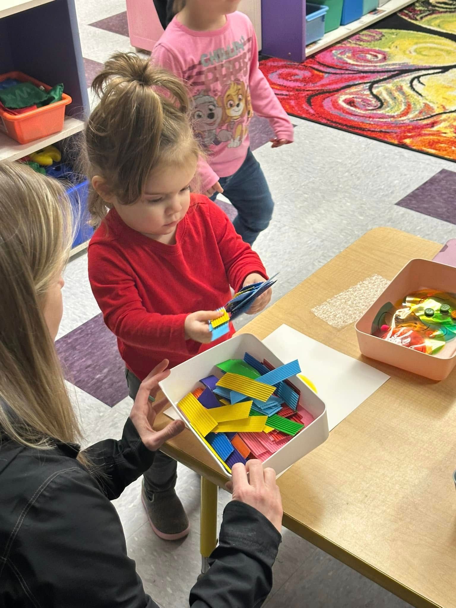 Child in red shirt sorting colorful craft sticks with an adult at a table.