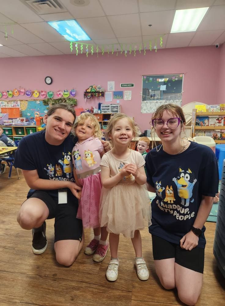 Two adults kneel with two young children in a classroom. All are smiling.