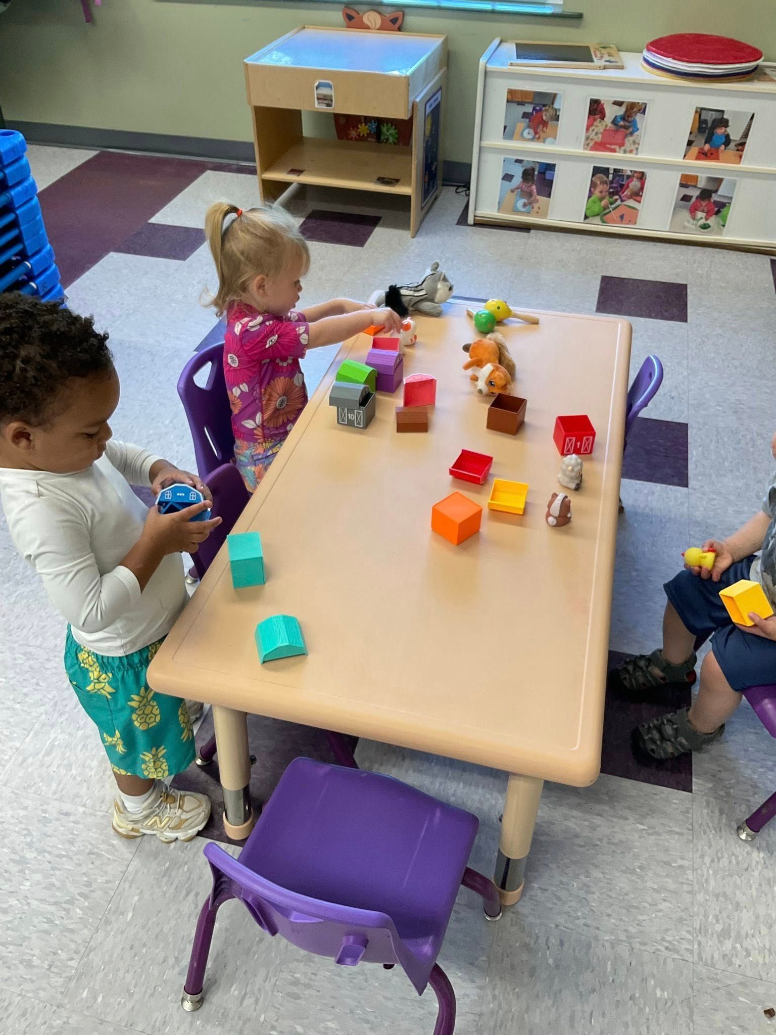 Children playing with blocks and toys at a table in a classroom.