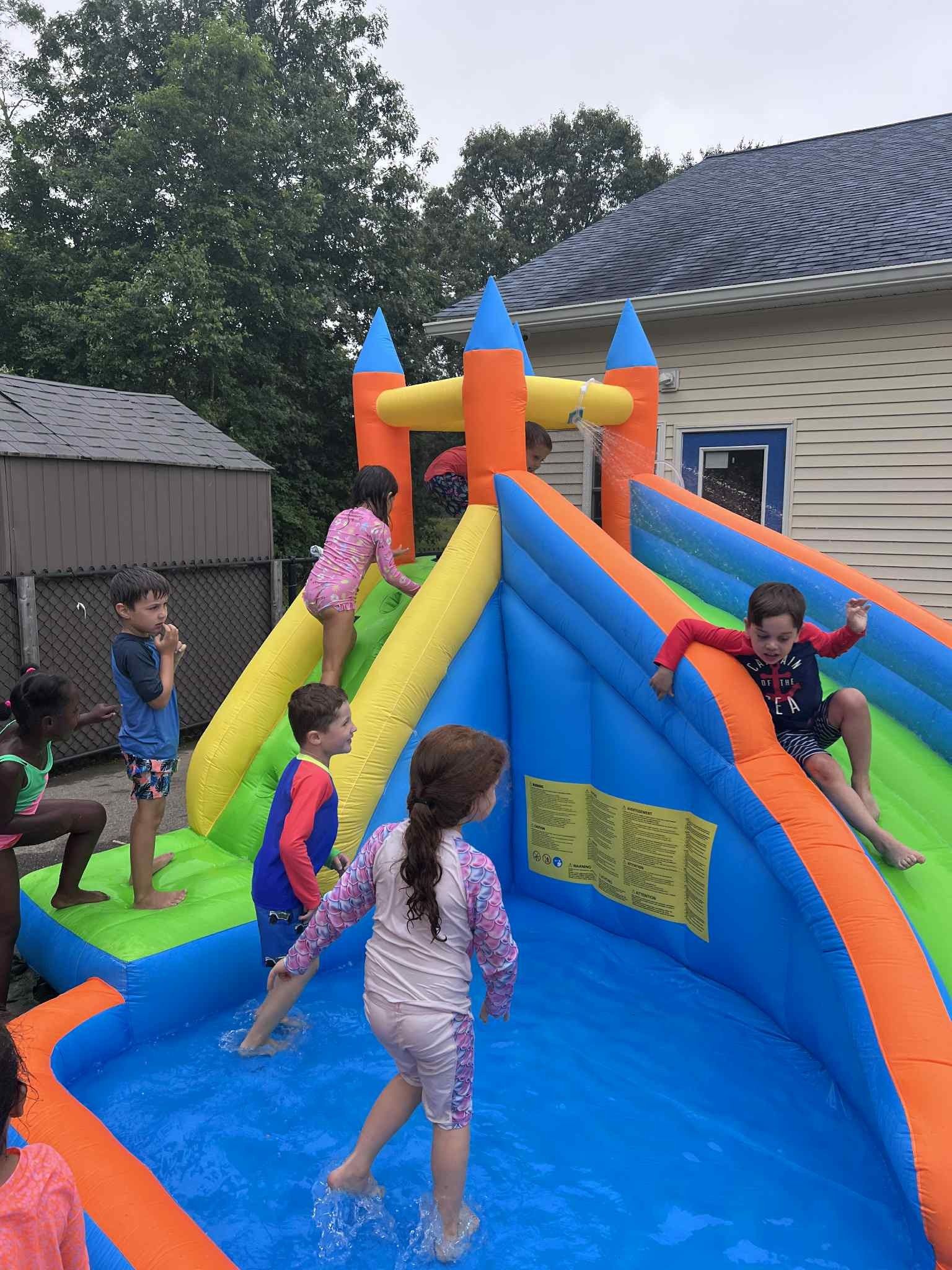 Children playing on a water slide and splash pool; blue, orange, and yellow inflatable castle.