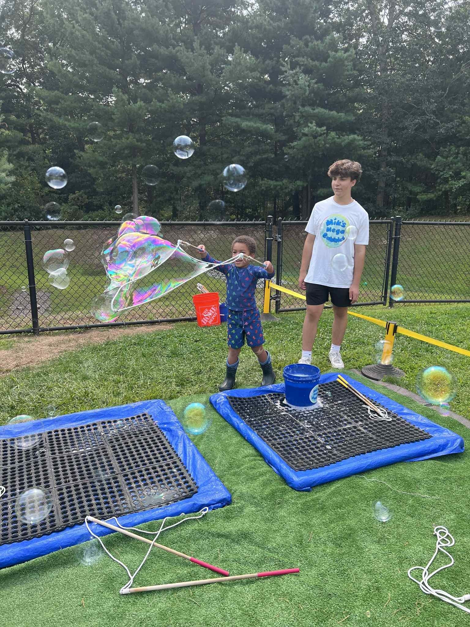 Two kids playing with bubbles outdoors: boy in jumpsuit catches bubbles, other stands nearby.