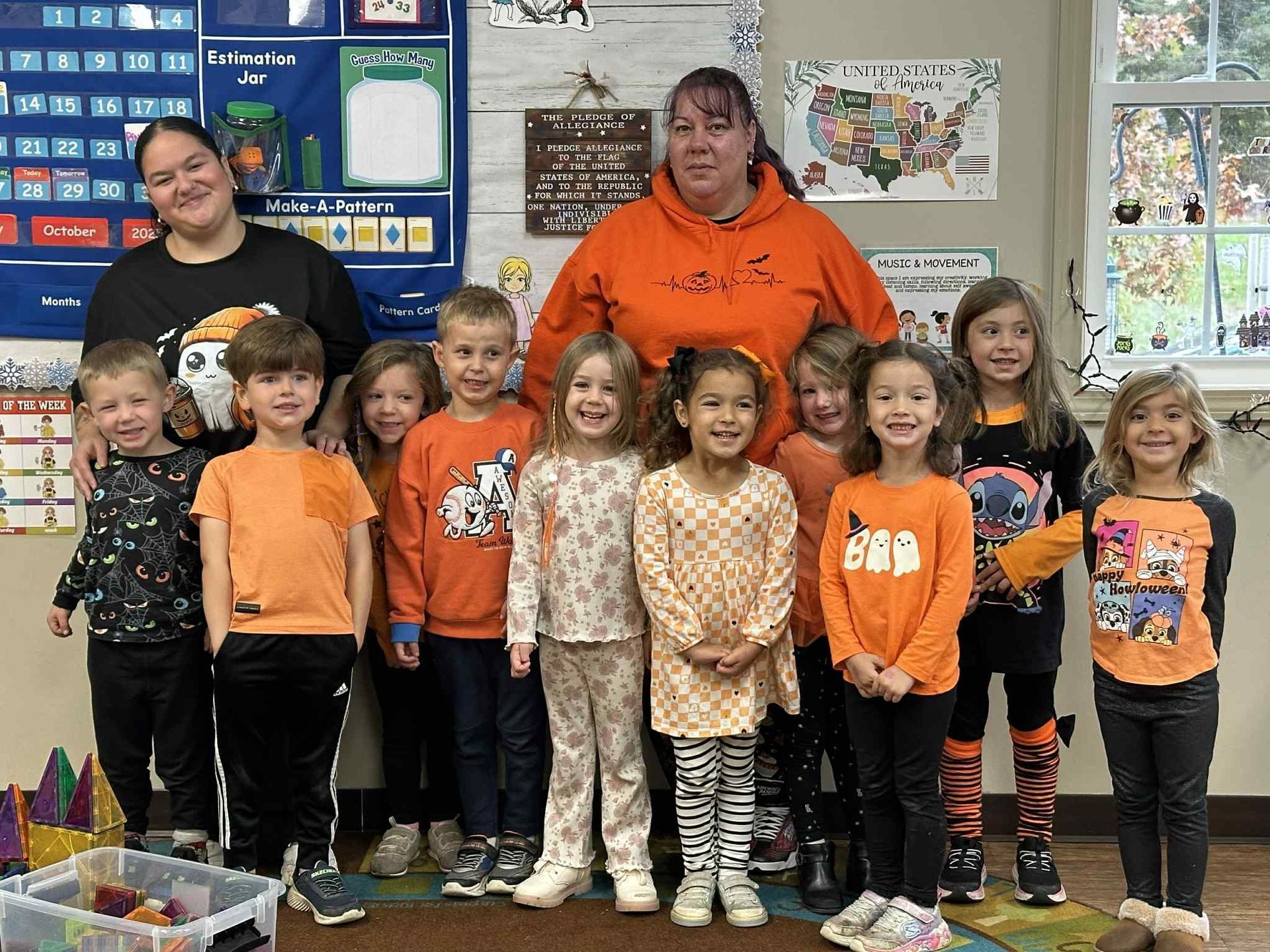 Two adults and ten children in orange clothing pose indoors.