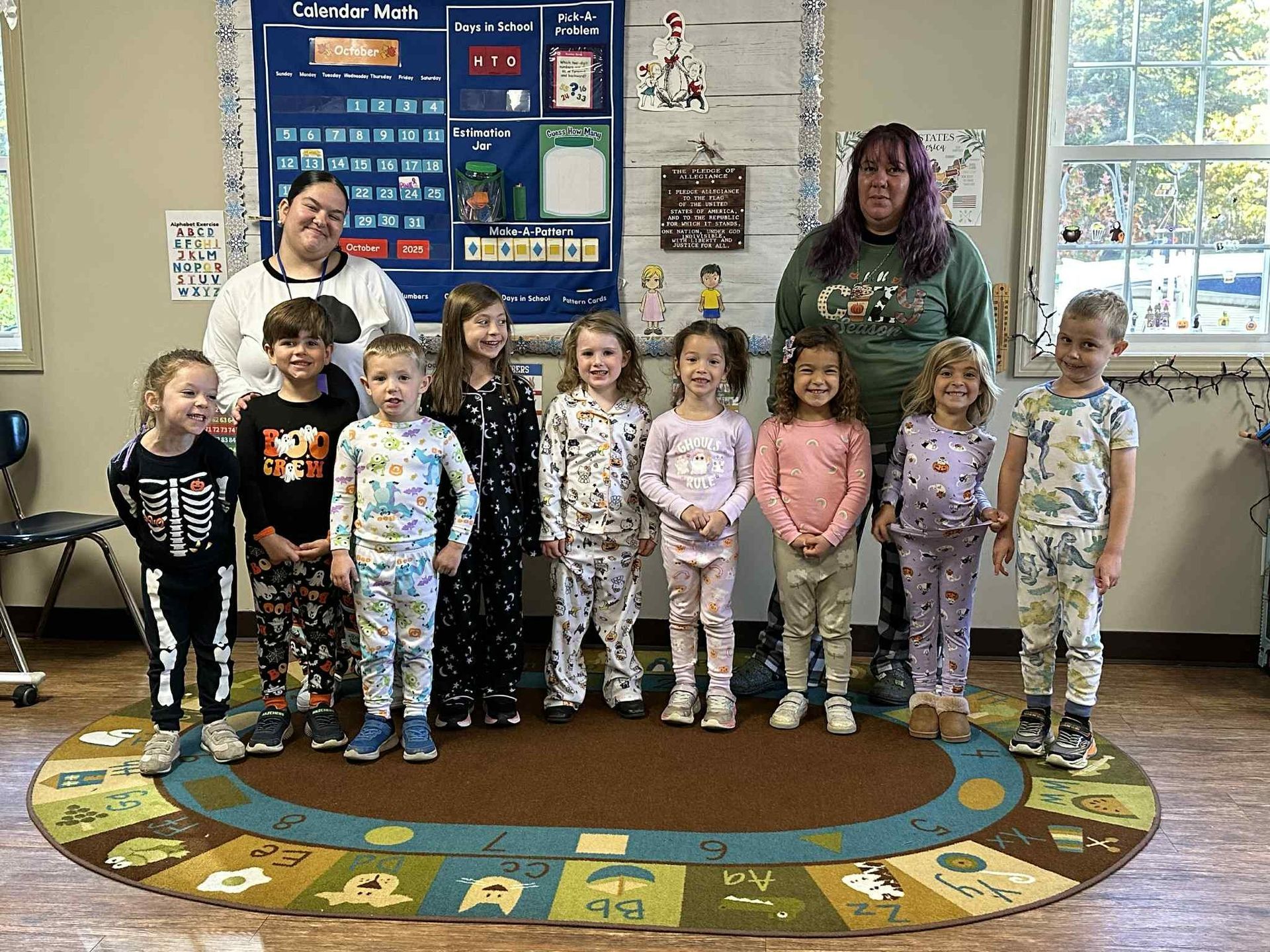 Children and two adults in a classroom; students wear pajamas.