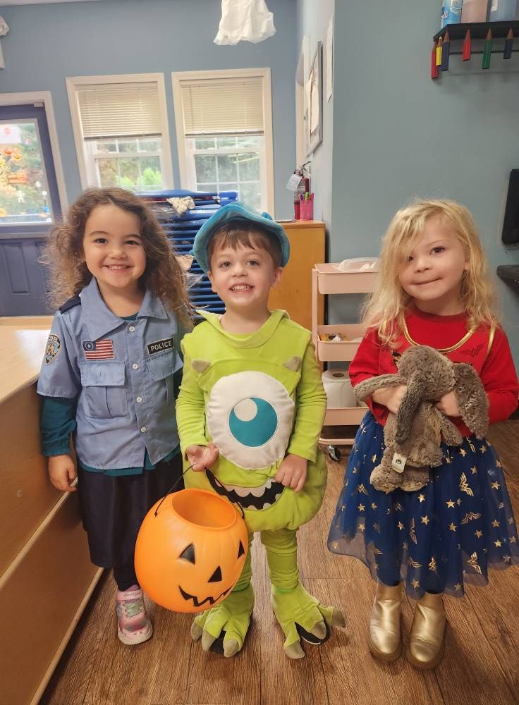 Three children in Halloween costumes smile indoors: a police officer, a monster, and a princess.