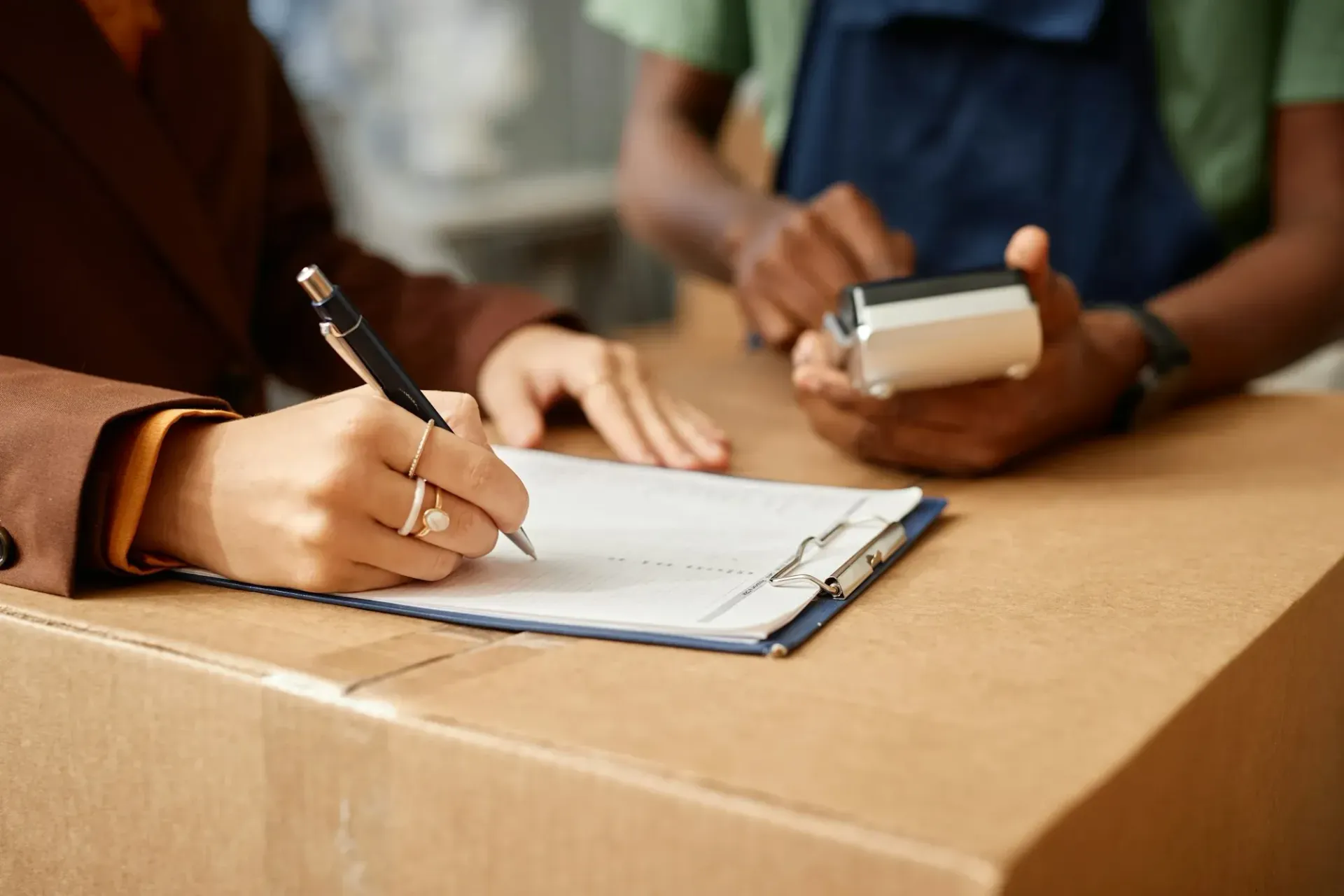 Person signing a document on a clipboard while another holds a smartphone at a table