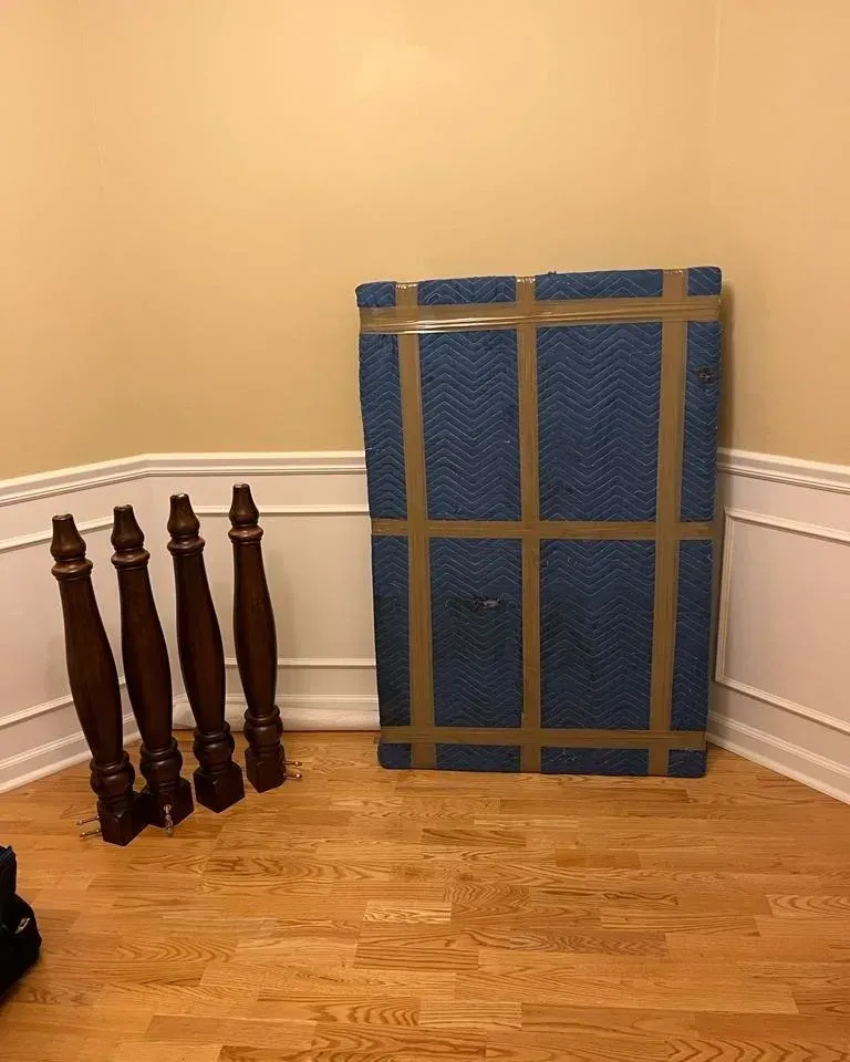 Blue foam mattress leaning against a beige wall beside dark wooden stair balusters on a hardwood floor