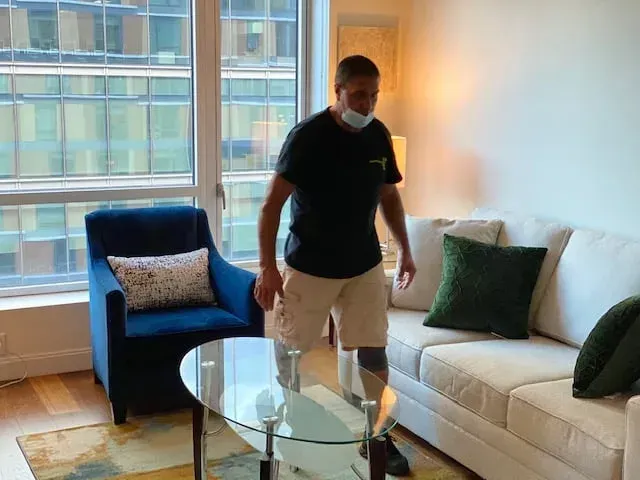Person standing in a bright living room beside a glass coffee table and white sofa.