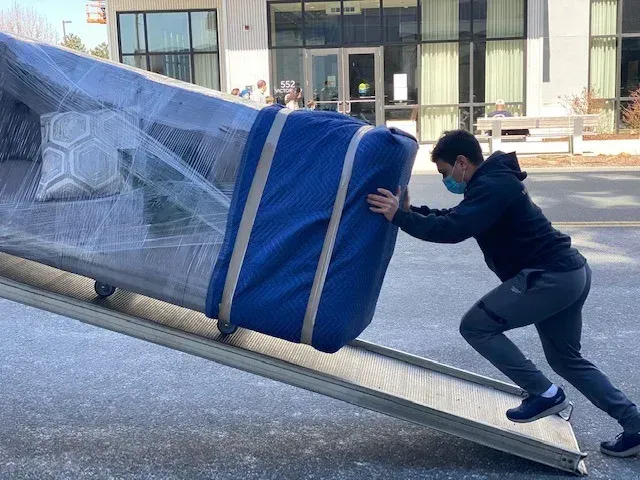 Person pushing a large wrapped object in a blue cover on a wheeled frame outdoors
