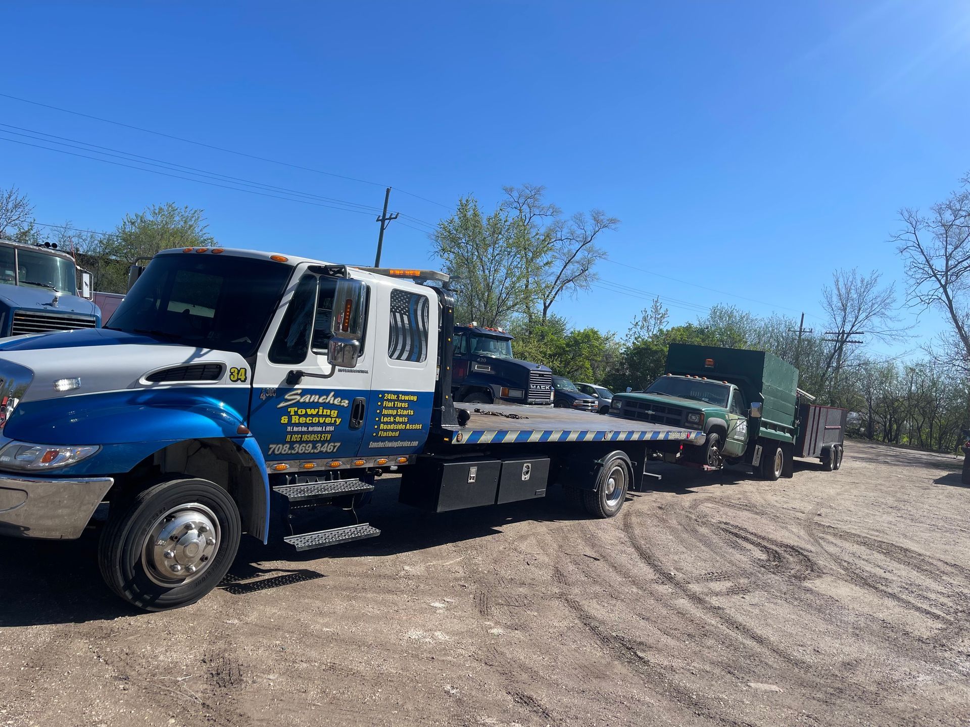 A blue and white tow truck is parked in a dirt lot.