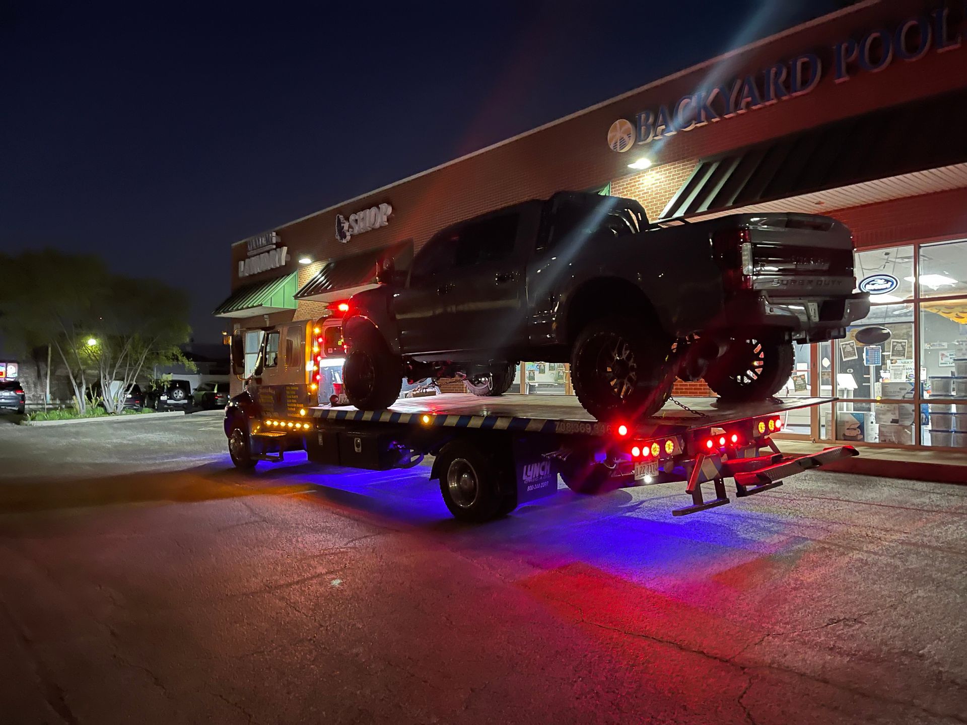 A truck is being towed by a tow truck at night.