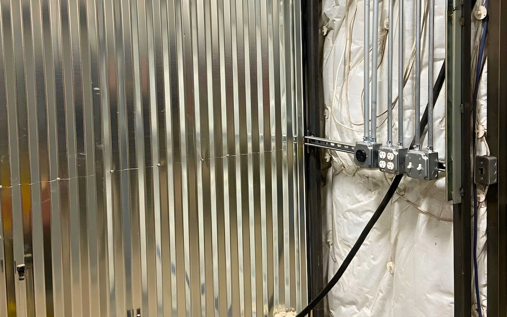 Galvanized metal wall with electrical conduit and outlets on a metal frame, against insulated wall.