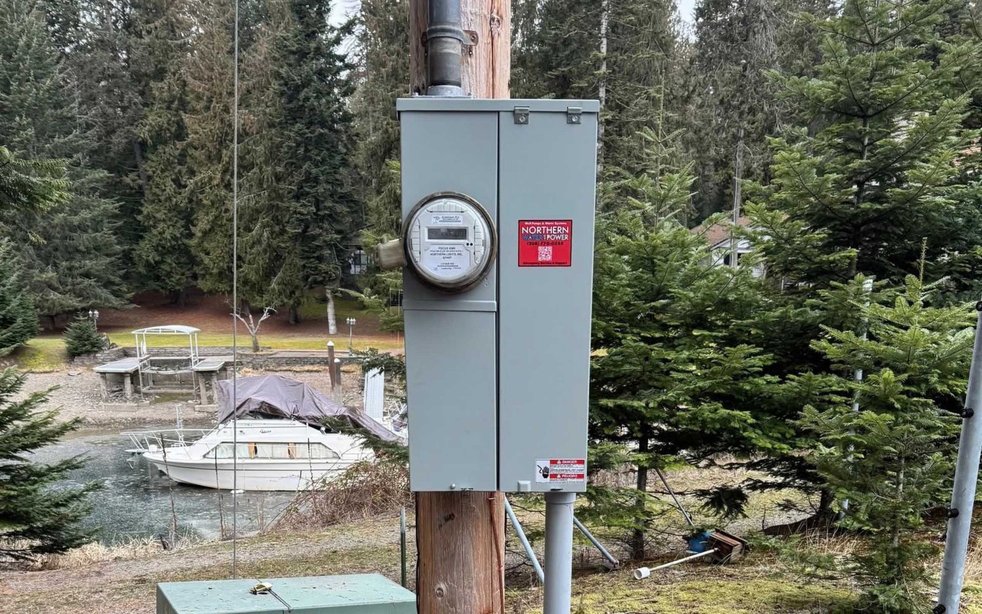 Electrical meter box on a utility pole with a boat and trees in the background.