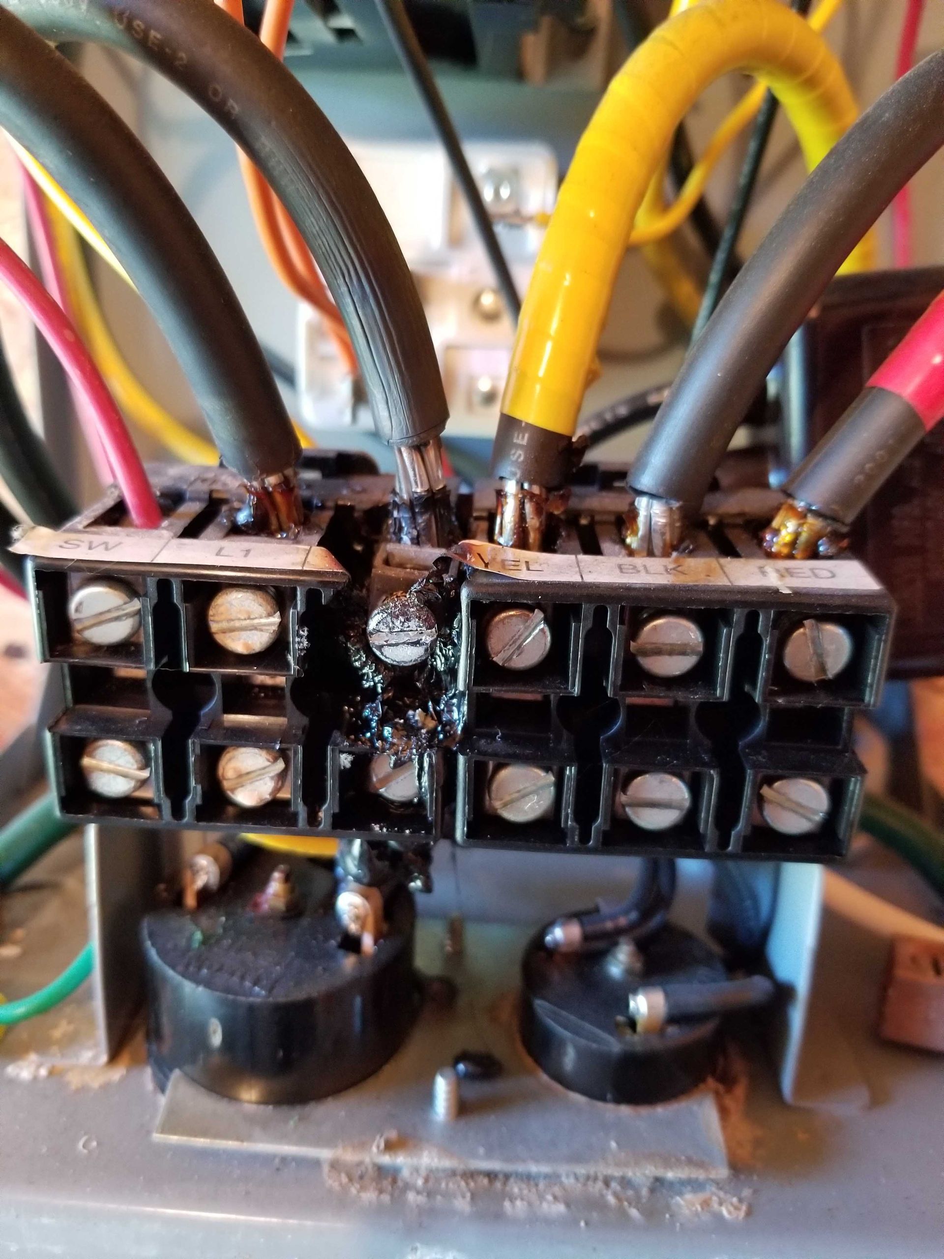 Burnt electrical component with several wires connected, showing charred plastic and exposed wiring.