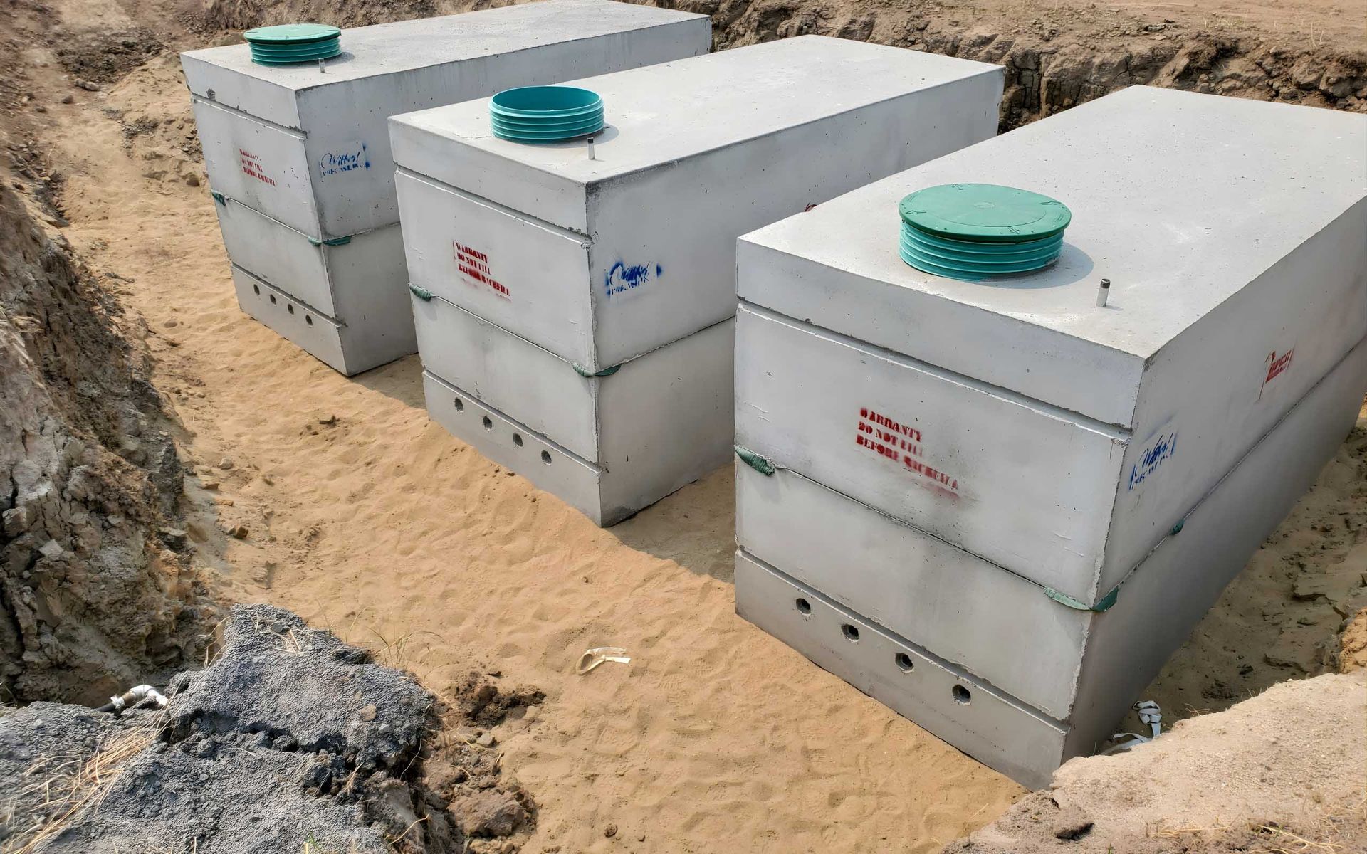 Three rectangular concrete septic tanks in a trench, ready for burial.