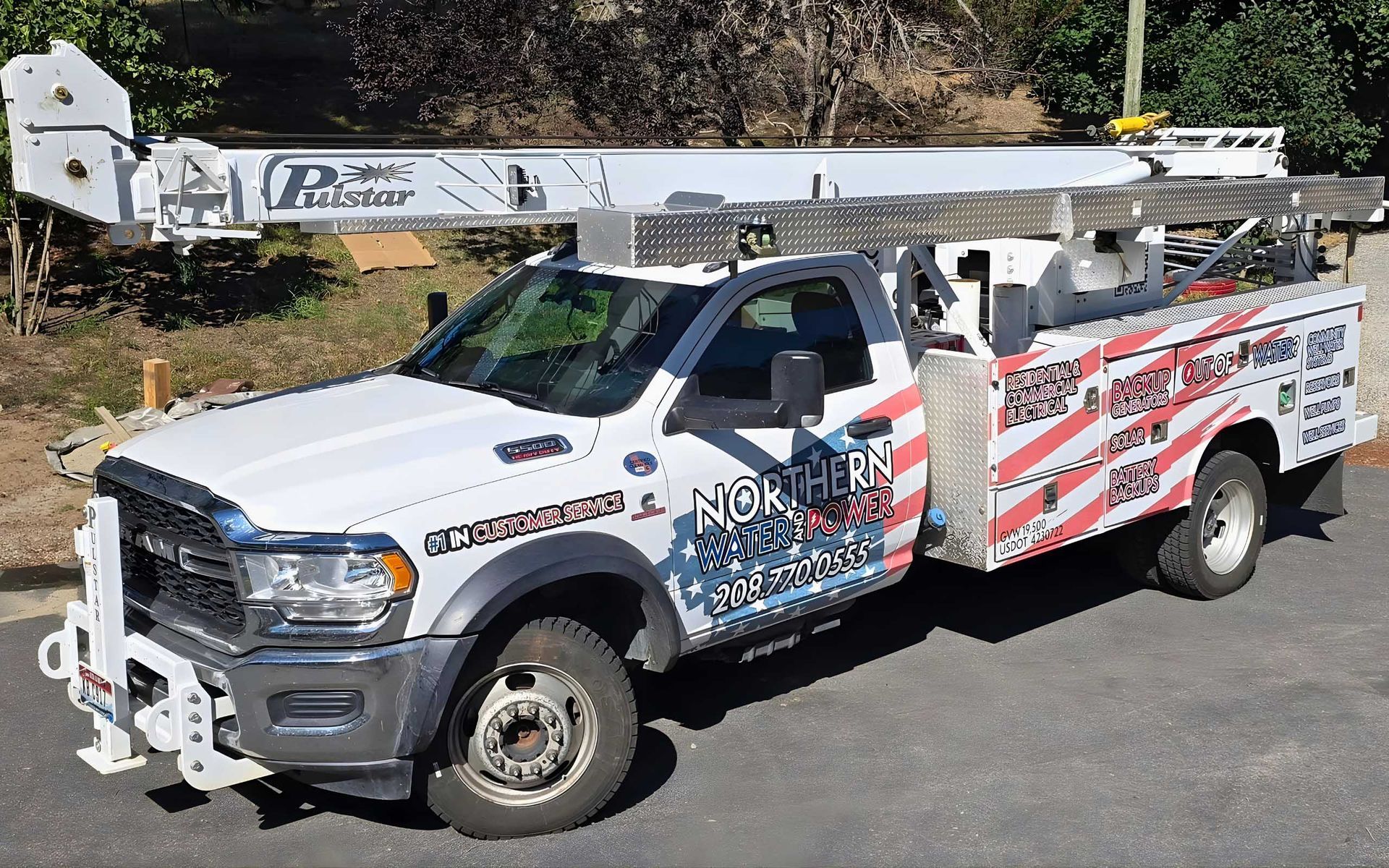White utility truck with boom lift, patriotic graphic, parked outdoors.