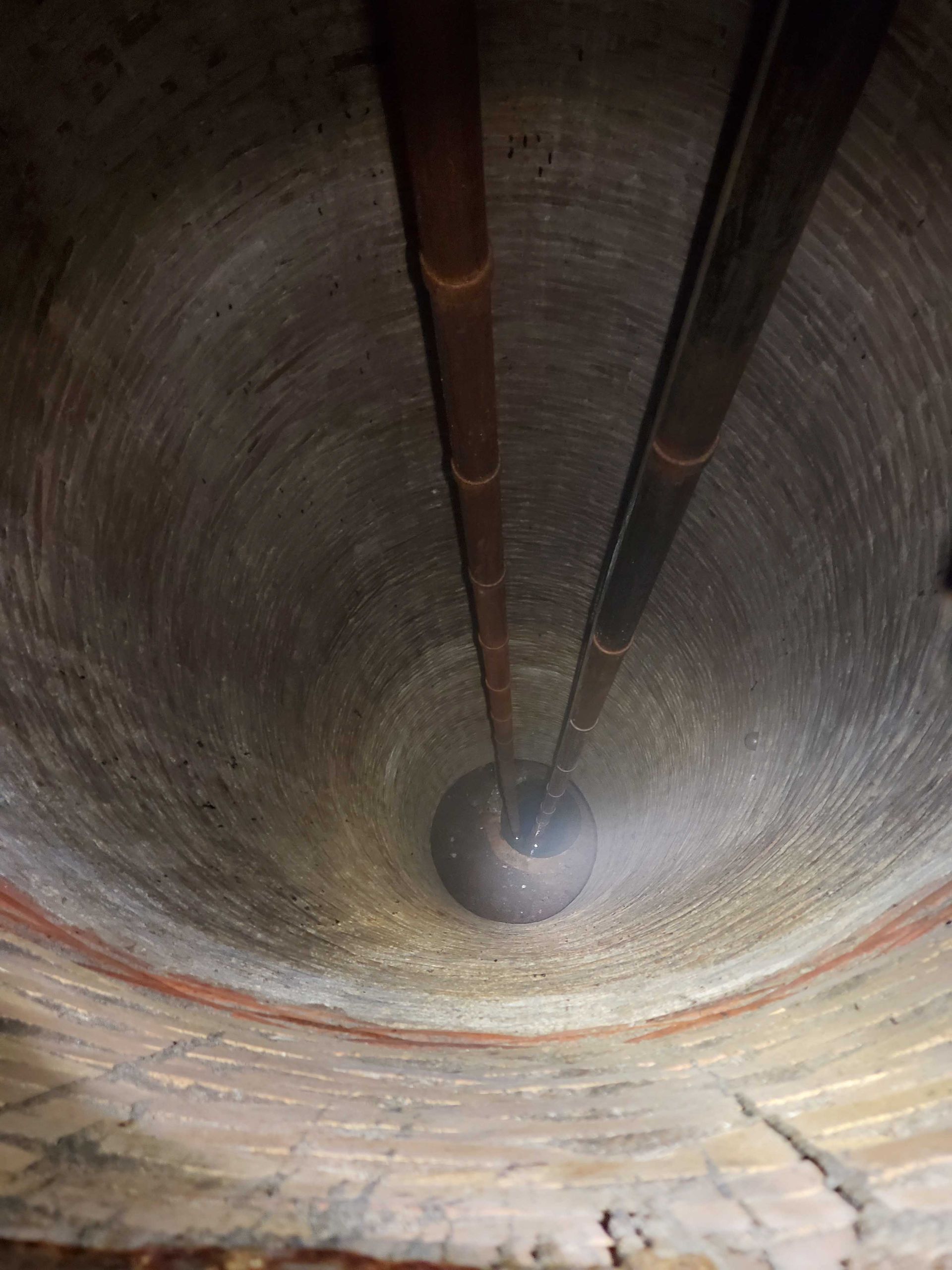 Inside of a deep, circular well. Two metal pipes extend down to a dark sphere at the bottom.