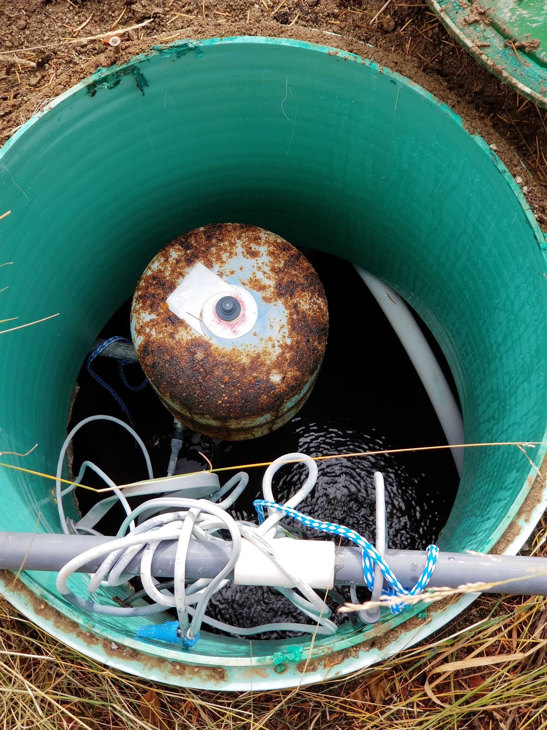 Septic tank interior with rusted float, wires, and dark liquid. Green tank with visible corrugation.