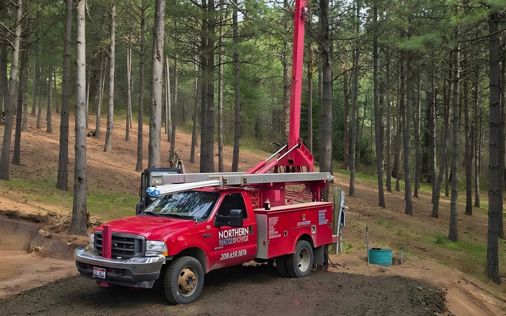 Red truck with drilling equipment in a forest, for water well work.