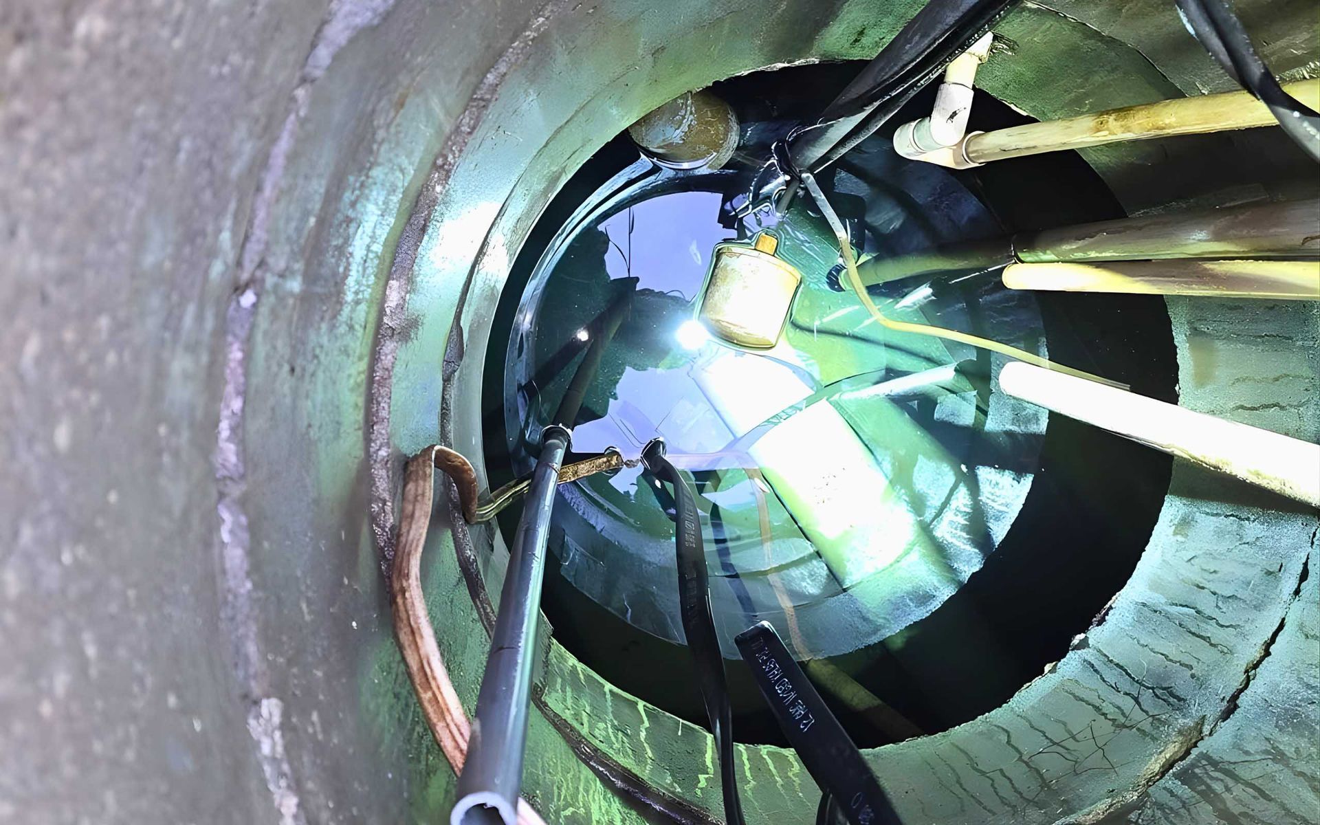 Looking down into a cylindrical well filled with water and equipment; cables and floats are visible.