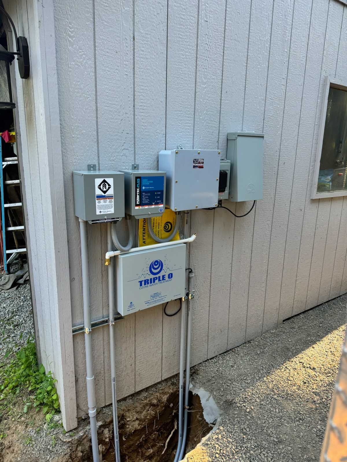 Electrical equipment mounted on a light-colored building exterior, with conduits leading into a trench.