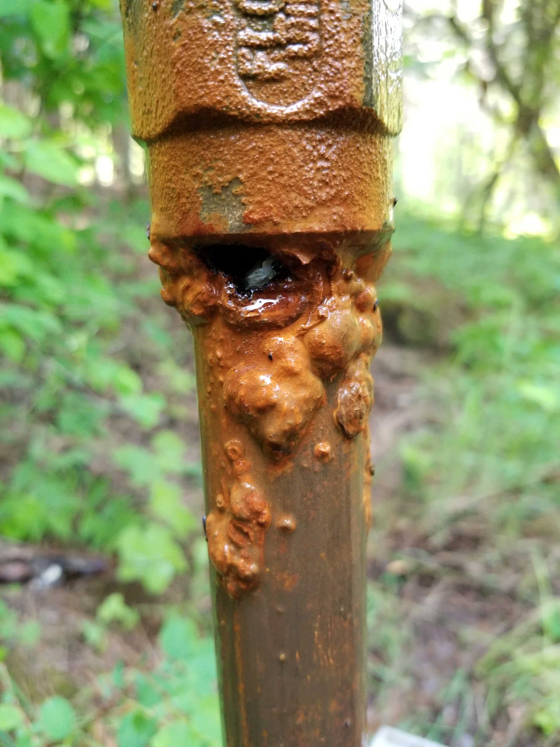 Rusty pipe with corrosion and hole. Brown and orange colors, outdoor setting.