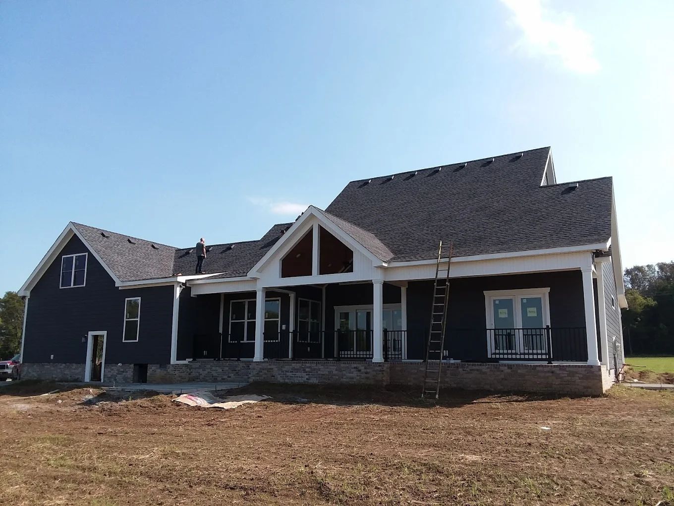 Dark blue house under construction; white trim, brown accents, and a dark roof against a blue sky.