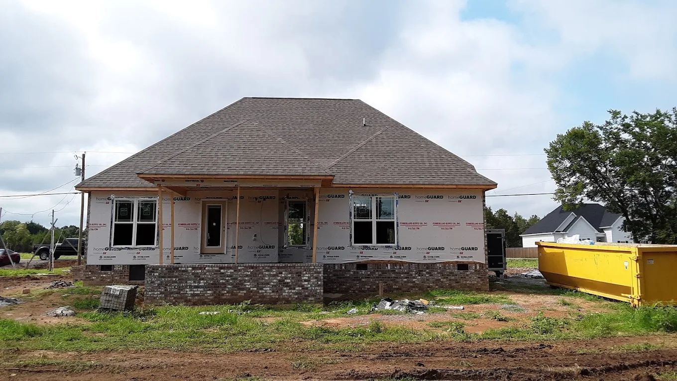 House under construction with brick facade, brown roof, windows, and a yellow dumpster.