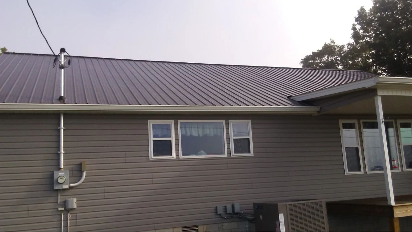 Grey house with a brown metal roof, white window frames, and grey siding.