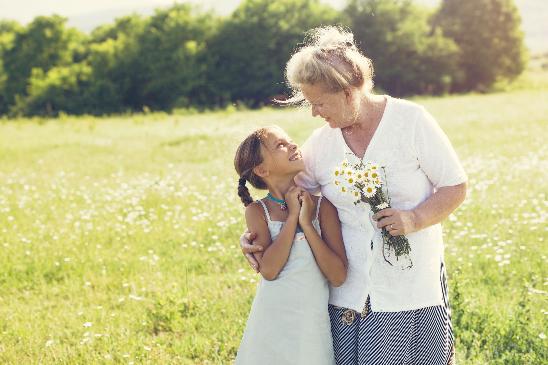 An elderly woman and a little girl are standing in a field holding hands.