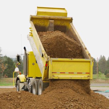 A yellow dump truck is dumping dirt into a pile