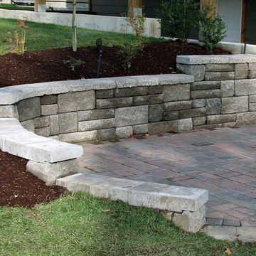 A stone wall surrounds a brick walkway in front of a house