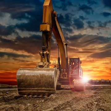 An excavator is working on a construction site at sunset.