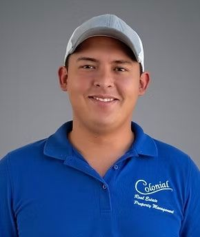 Smiling person in a blue polo and gray cap against a plain gray background
