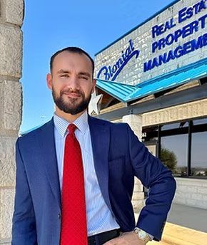 Man in navy suit and red tie standing outside a real estate property management office