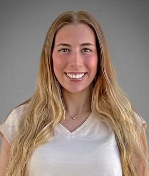 Portrait of a smiling person with long blonde hair wearing a white shirt against a gray background