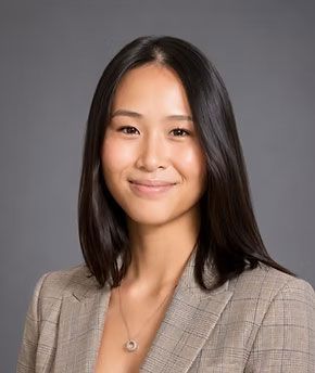 Portrait of a smiling person in a beige blazer against a gray background