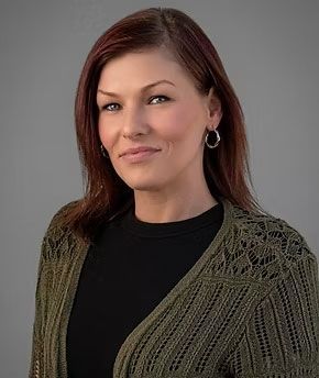 Portrait of a woman with shoulder-length brown hair, wearing a black top and olive knit cardigan on a gray background