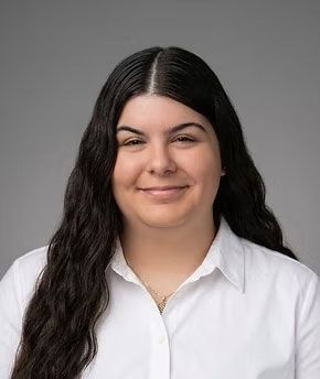 Smiling person with dark hair wearing a white shirt against a gray background