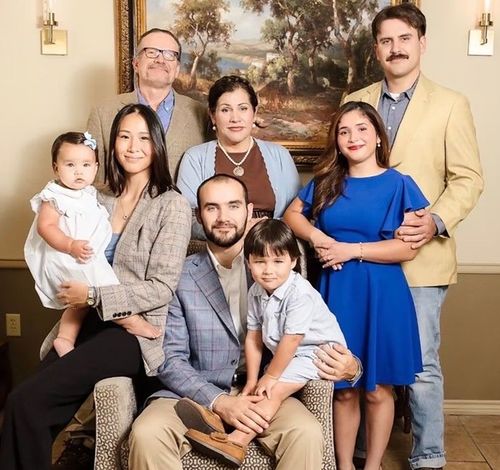Family portrait of seven adults and two children posed indoors in front of a framed painting
