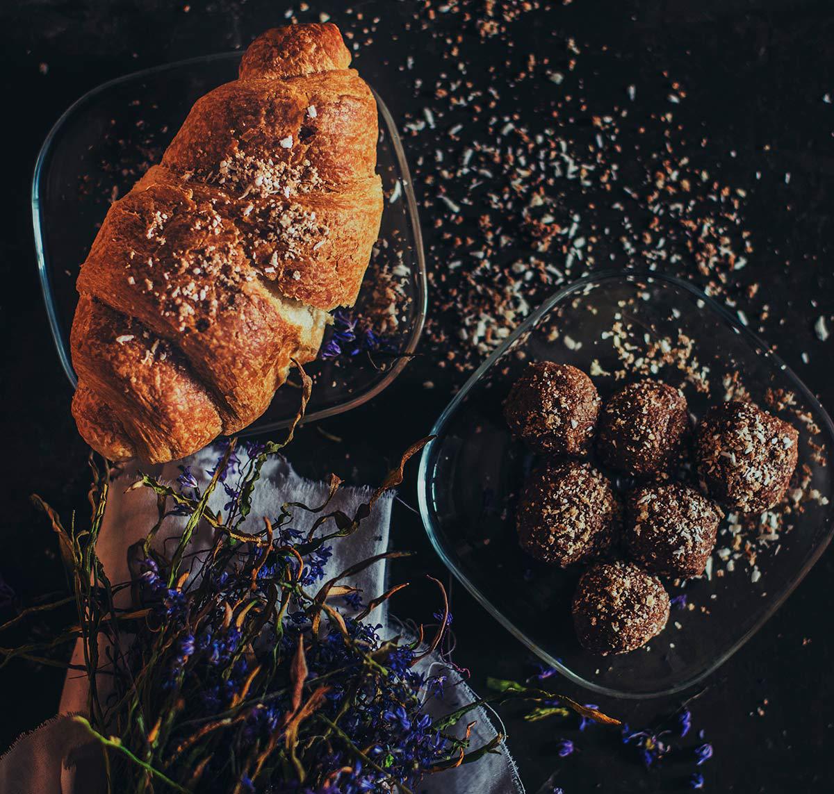 Croissant and chocolate truffles on dark plates, with purple flowers on a dark background