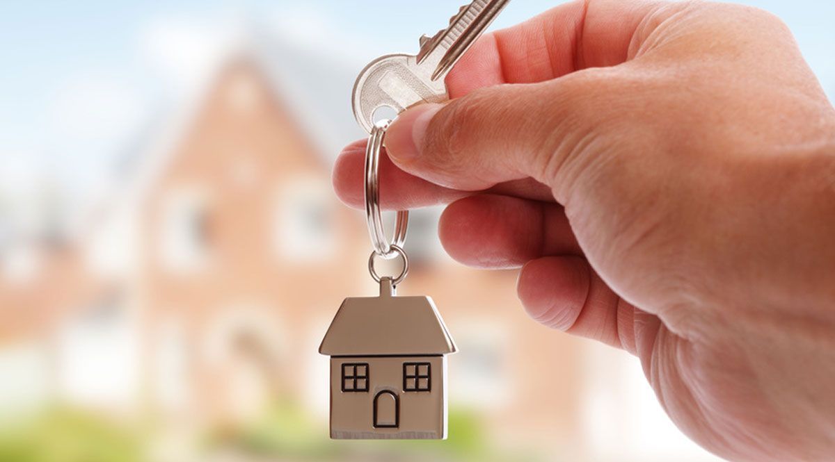 Hand holding house key with small house keychain, blurred house in background